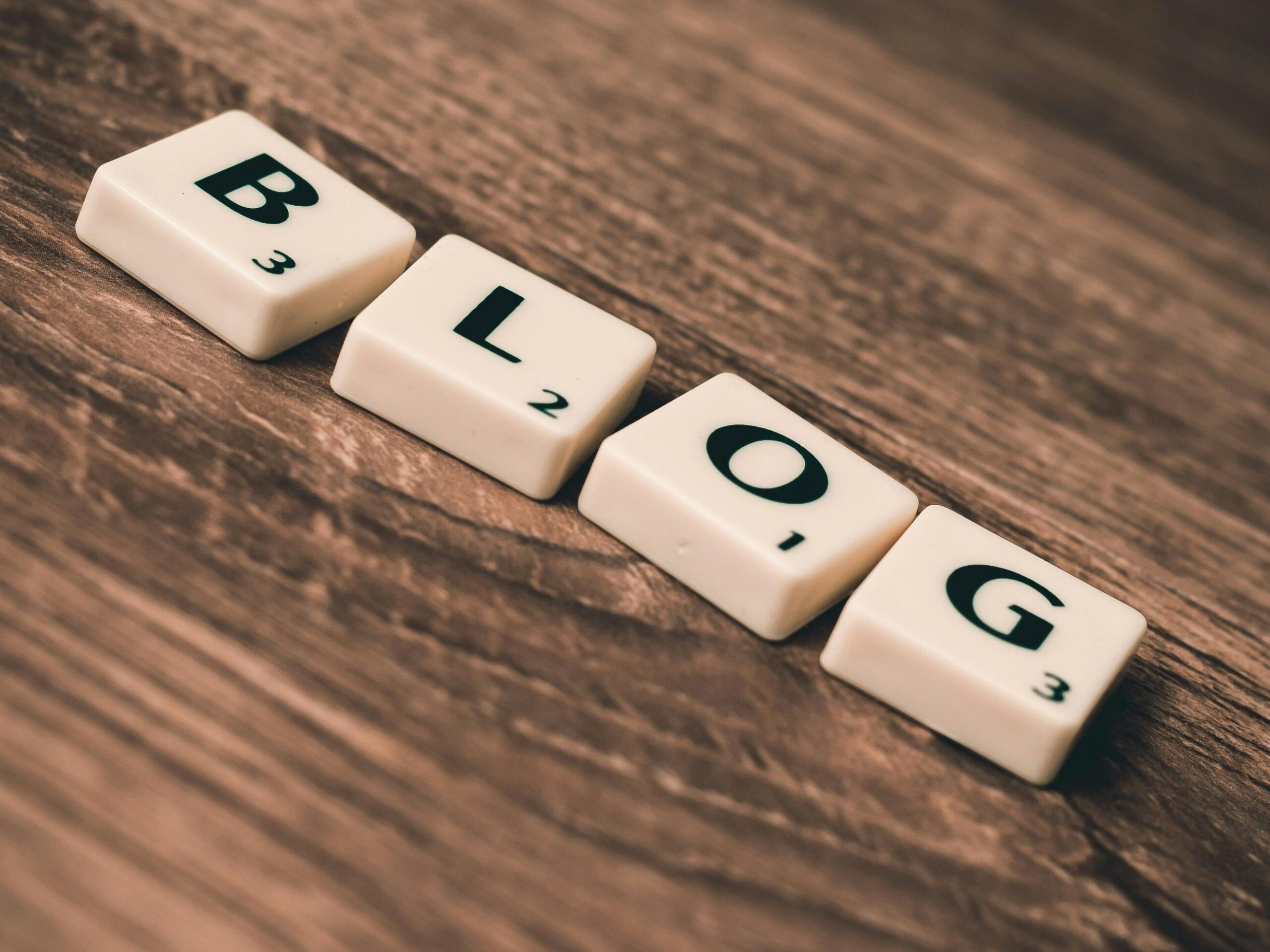 Scrabble tiles spelling 'BLOG' on a wooden background, symbolizing creativity and writing.